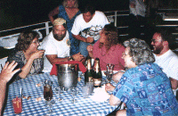 [ Image: A picture of Julie, Jeff, and others sitting around
             a table on deck talking and drinking champagne ]